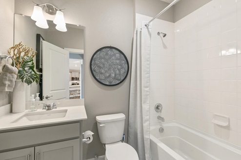 gray cabinet bathroom with a dual-basin sink and a tub and toilet