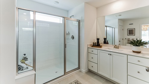 Primary bathroom with large glass door shower and sitting bench inside.