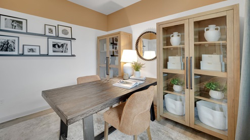 Secondary bedroom set up as an office with a desk with chairs on each side, two glass-fronted bookshelves, and picture rails displaying family photos on the back wall.
