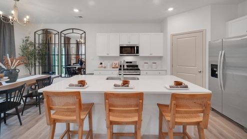 A spacious kitchen with white, shaker-style cabinets, quartz countertops, a large center island with undermount sink and seating for three, and a stainless-steel appliance package.