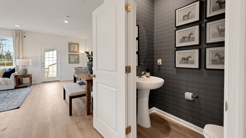 First floor hallway from the foyer with view of the half bath and part of the living area and dining area.