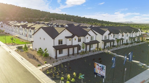 A row of beautiful modern white townhomes with black roofs and trim with luscious green grass laid out in front of them.