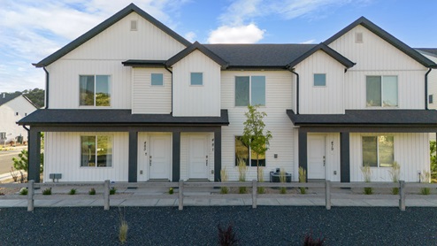 A row of beautiful modern white townhomes with black roofs and trim with luscious green grass laid out in front of them.