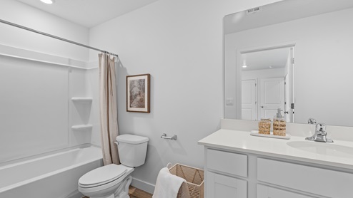 Primary bedroom’s ensuite full size bathroom with white cabinets and tub shower combination.