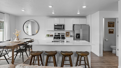Focusing on the kitchen there is a large island with sink, white shaker cabinets and stainless steel appliances.