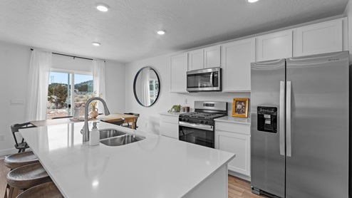 Focusing on the kitchen there is a large island with sink, white shaker cabinets and stainless steel appliances.