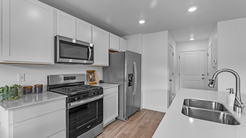 A wide entryway through the kitchen with white countertops and shaker cabinets, stainless steel appliances and a large island with a sink.