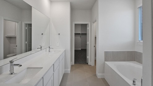Spacious modern bathroom featuring a glass-enclosed shower, a large soaking tub with tiled surround and dual-sink vanity with sleek countertop. The layout includes a private water closet and a walk-in closet for added convenience, with natural light streaming through the window.