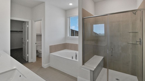Spacious modern bathroom featuring a glass-enclosed shower, a large soaking tub with tiled surround and dual-sink vanity with sleek countertop. The layout includes a private water closet and a walk-in closet for added convenience, with natural light streaming through the window.