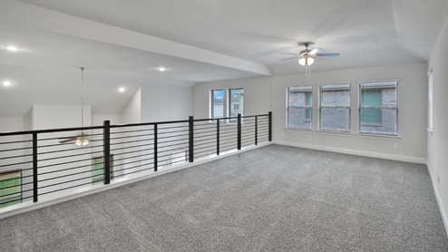Bright and airy loft area with carpeted flooring, modern railing, and ceiling fan lighting. The open design overlooks the main living space below, creating a perfect spot for relaxation or additional living space.