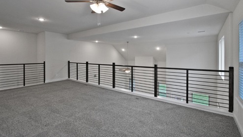 Bright and airy loft area with carpeted flooring, modern railing, and ceiling fan lighting. The open design overlooks the main living space below, creating a perfect spot for relaxation or additional living space.