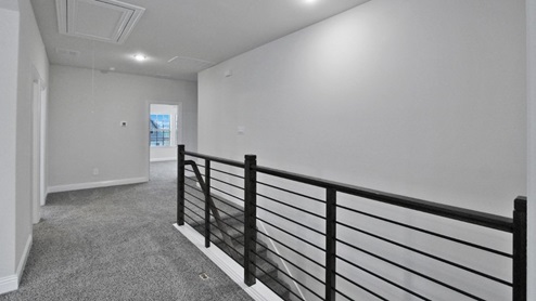 Bright and airy loft area with carpeted flooring, modern railing, and ceiling fan lighting. The open design overlooks the main living space below, creating a perfect spot for relaxation or additional living space.