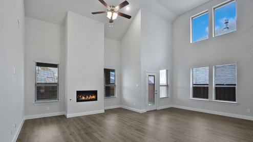 Modern open-concept living room with cozy fireplace, large windows offering natural light, and wood-look flooring. The space features a contemporary staircase with sleep railing leading to an upper loft area, and a view of the bright kitchen with white cabinetry, stainless steel appliances, and a spacious island.