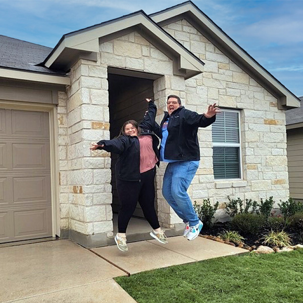 Husband and wife jumping in front of new house