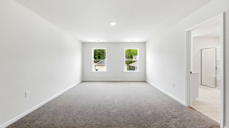 Primary bedroom with carpet and windows.