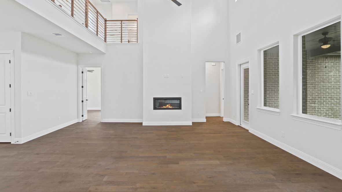 Spacious living room with brown flooring, white walls, a black fireplace and windows