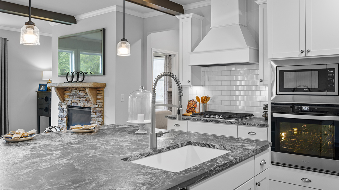 ashley model home kitchen with stainless steel appliances, pendant lights, and dark granite countertops