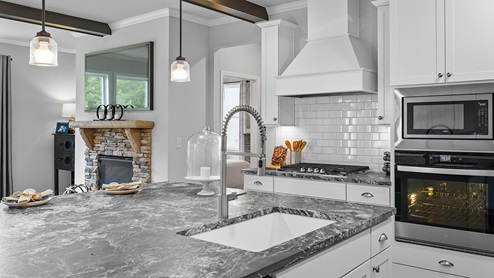 ashley model home kitchen with stainless steel appliances, pendant lights, and dark granite countertops