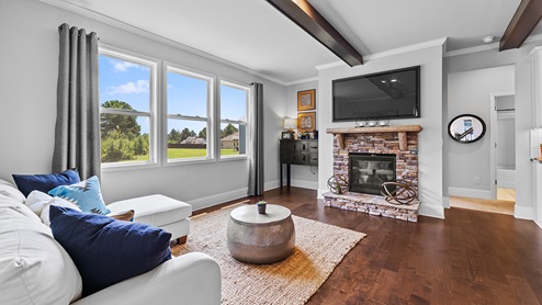 ashley model home living room with stacked stone fireplace, exposed beams, and large windows
