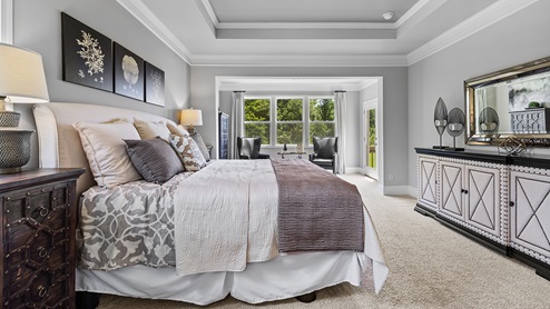ashley model home primary suite bedroom with extra sitting room, tray ceilings, and access to the back deck