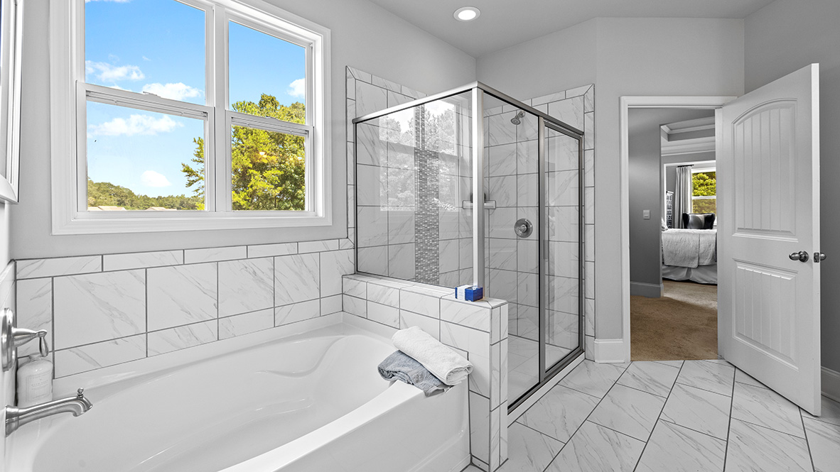 ashley model home primary suite tiled bathroom with separate soaking tub and tiled walk-in shower and walk-in closet
