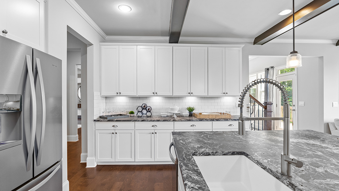 ashley model home kitchen with dark granite countertops, white cabinets, and exposed beams