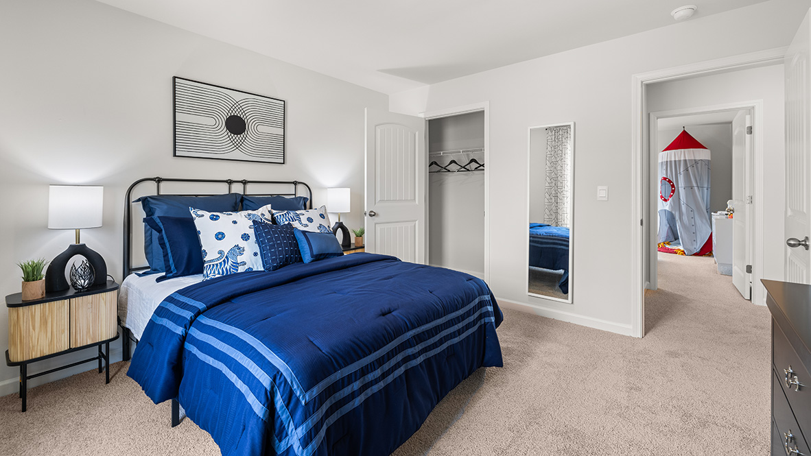 Secondary bedroom in Hanover Plan with neutral paint tones and closet storage crafted by D.R. Horton in Dallas Georgia with blue bed, carpeted floor