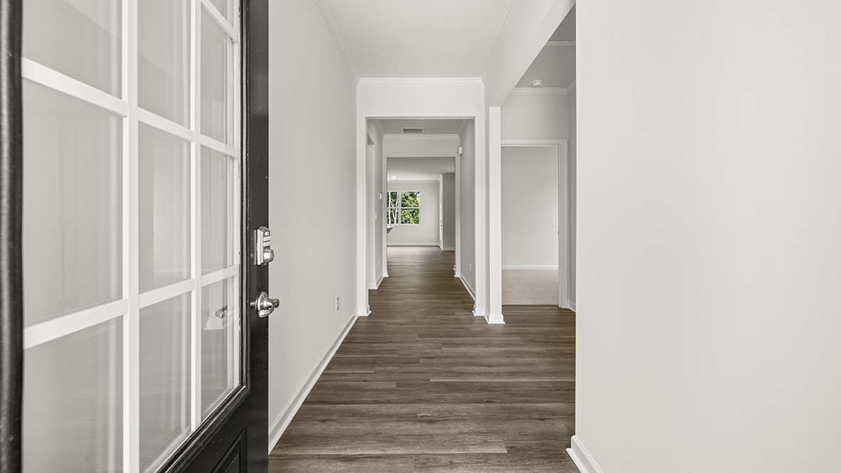 Entry hallway in this New Construction Home by D.R. Horton features a long corridor with guest bedroom access on the left and sightlines into the Open Concept kitchen and family room