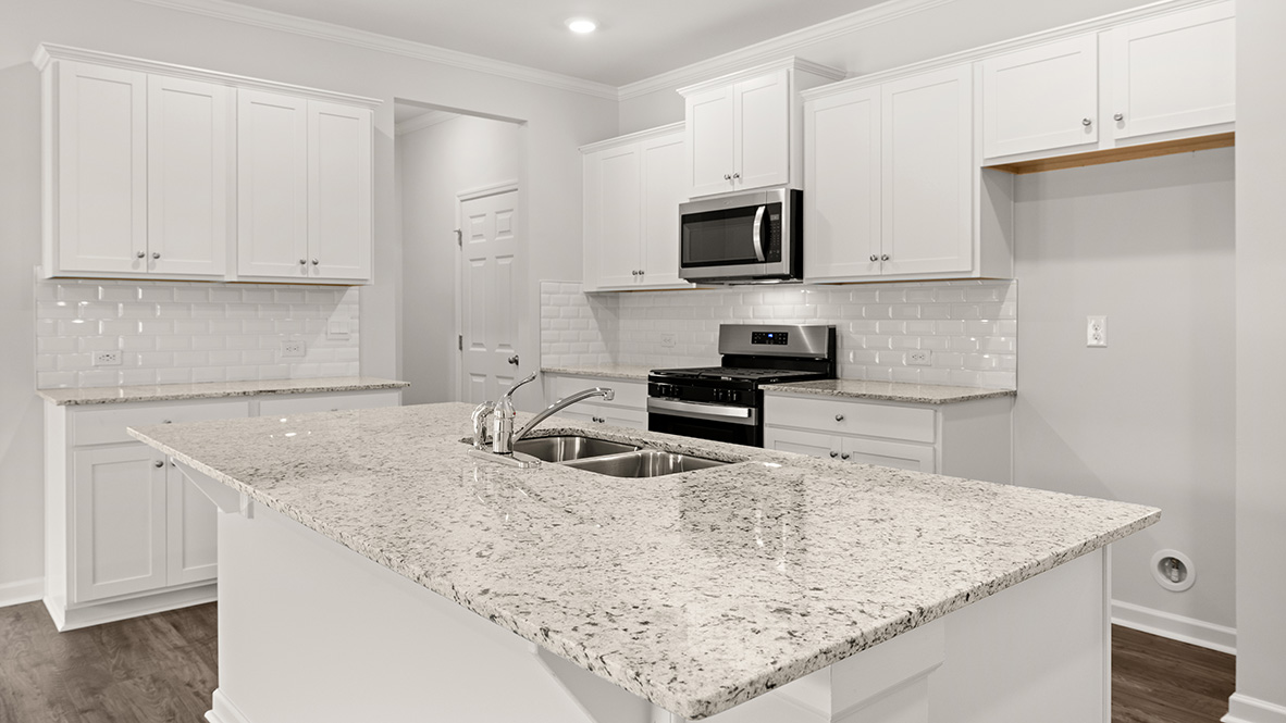 Open-concept kitchen with white cabinetry and a center island, overlooking the living area with fireplace and large windows.