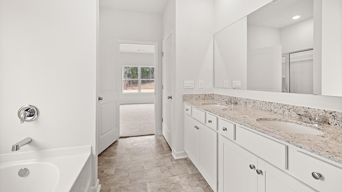 Primary bathroom featuring dual-sink vanity, white cabinetry, and access to a walk-in closet.