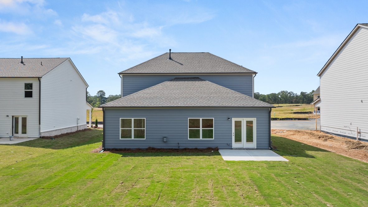 Rear view of two-story house with white siding and large backyard.