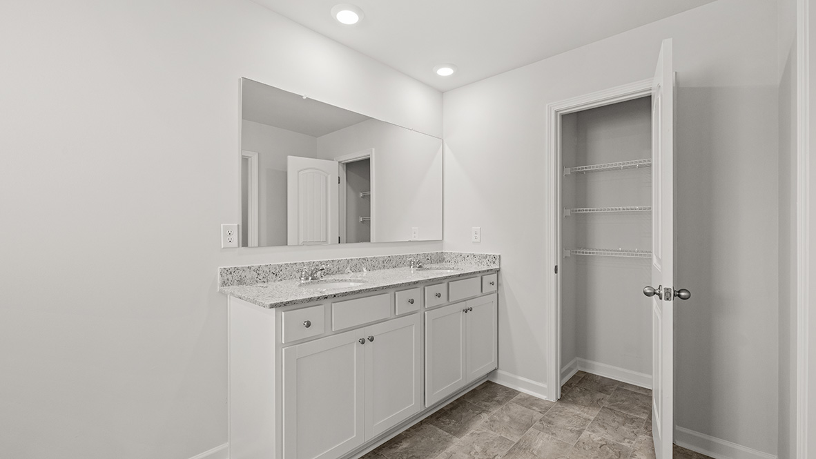 eslton primary suite bathroom with a granite dual vanity and tiled flooring