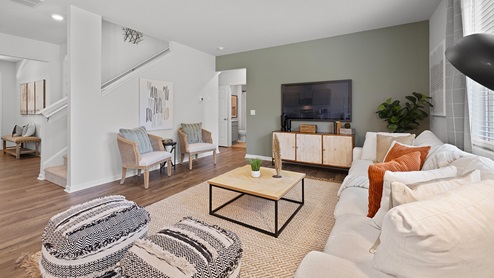 hayden model home open concept living room with a green accent wall open to the kitchen and stairway