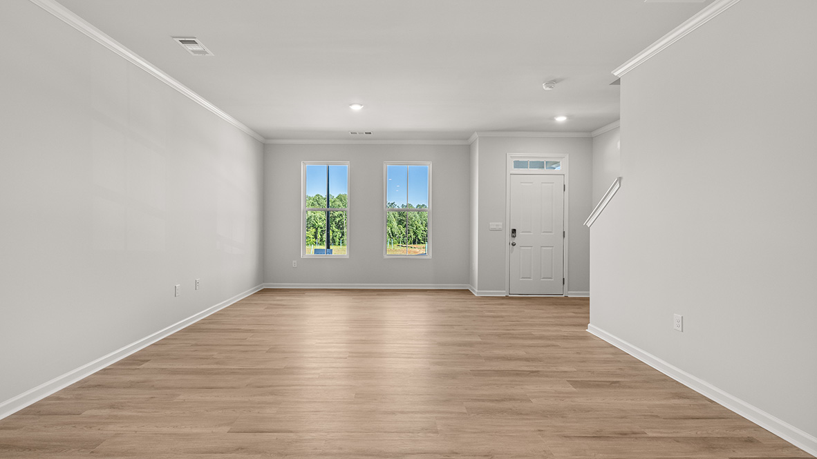 Spacious living room with brown flooring, white walls and windows