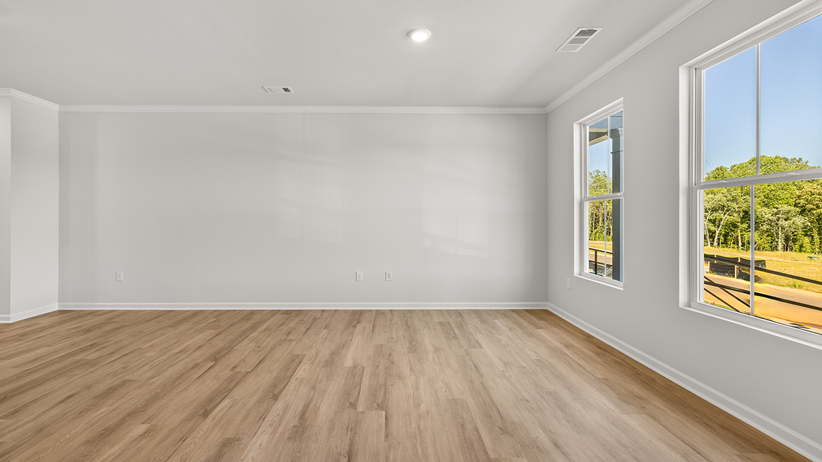 Spacious living room with brown flooring, white walls and windows