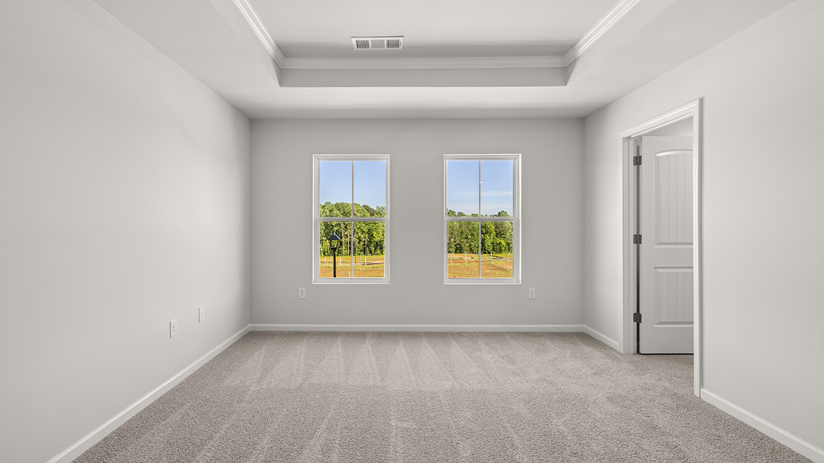 Spacious primary bedroom with beige carpet, white walls and two windows