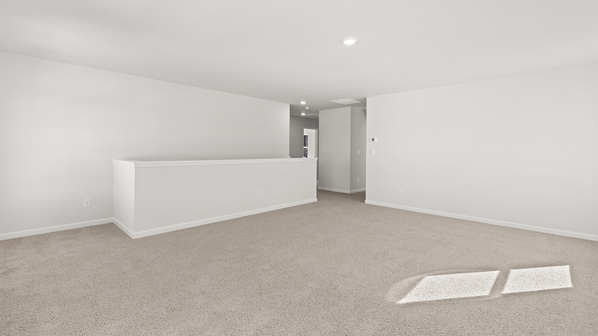 Upstairs living area with neutral carpet and a view of the stairs, and a hallway to the bedrooms.