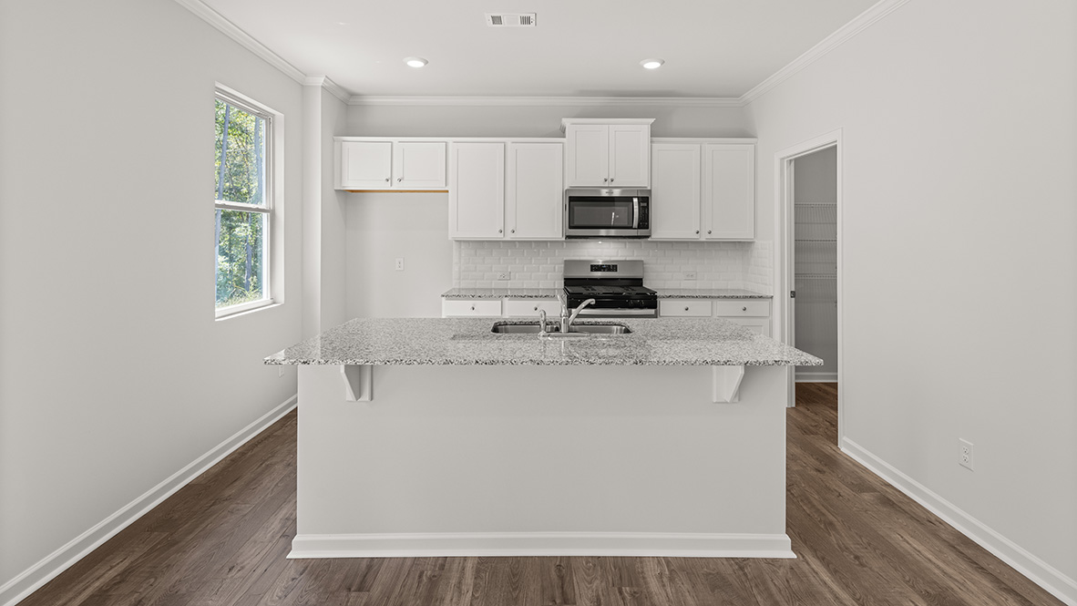 View of the kitch from the living room. The kitchen has granite countertops, white shaker-style cabinets, white subway tile backsplash and stainless steel appiances.