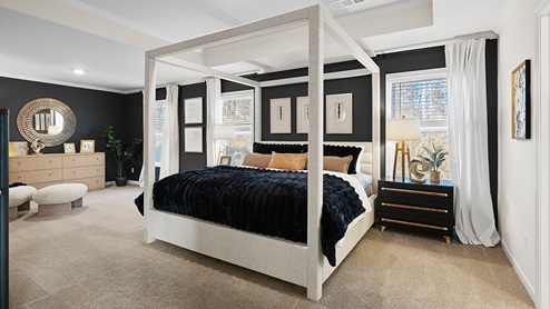 Butner Estates community model home primary suite bedroom with light carpet and two large windows for natural light