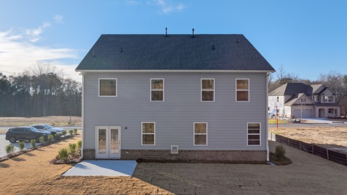 Rear exterior of home with concrete slab and large backyard.