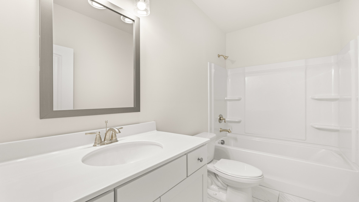 New House secondary bathroom in Butner Estates includes vanity, hard surface countertop, and storage cabinetry crafted by D.R. Horton