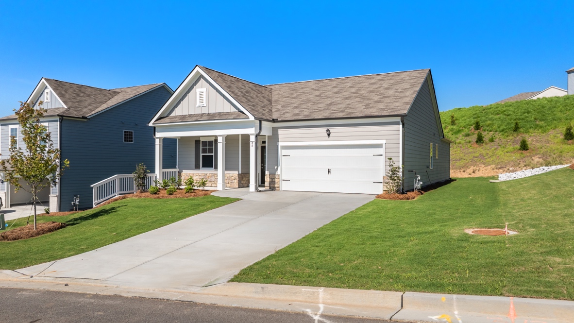 Angled view of single-story house with covered porch, driveway, and landscaped yard.