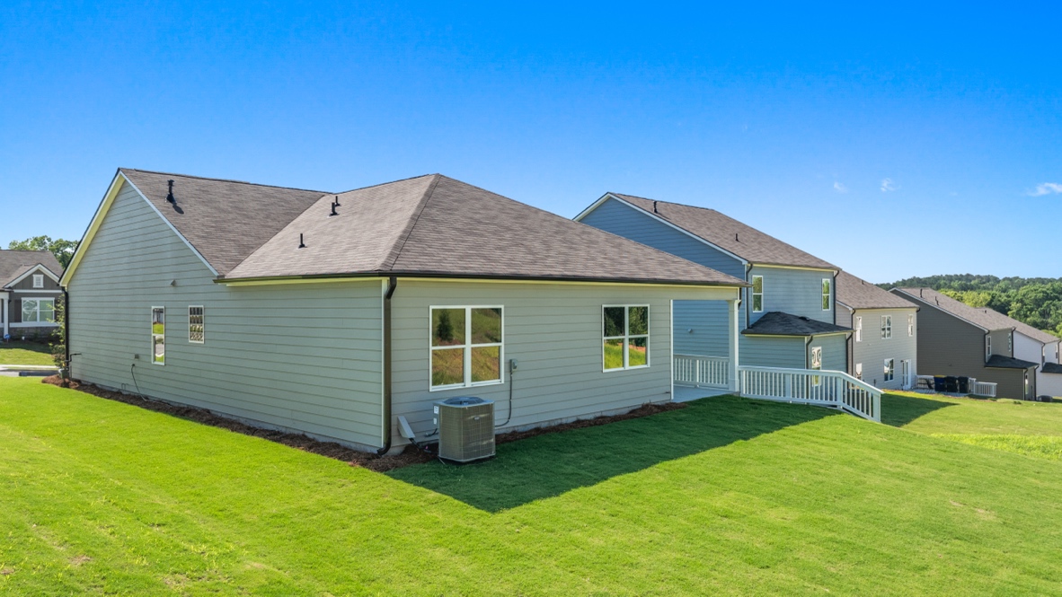 Rear exterior of single-story house with windows, small porch, HVAC unit, and grassy yard.