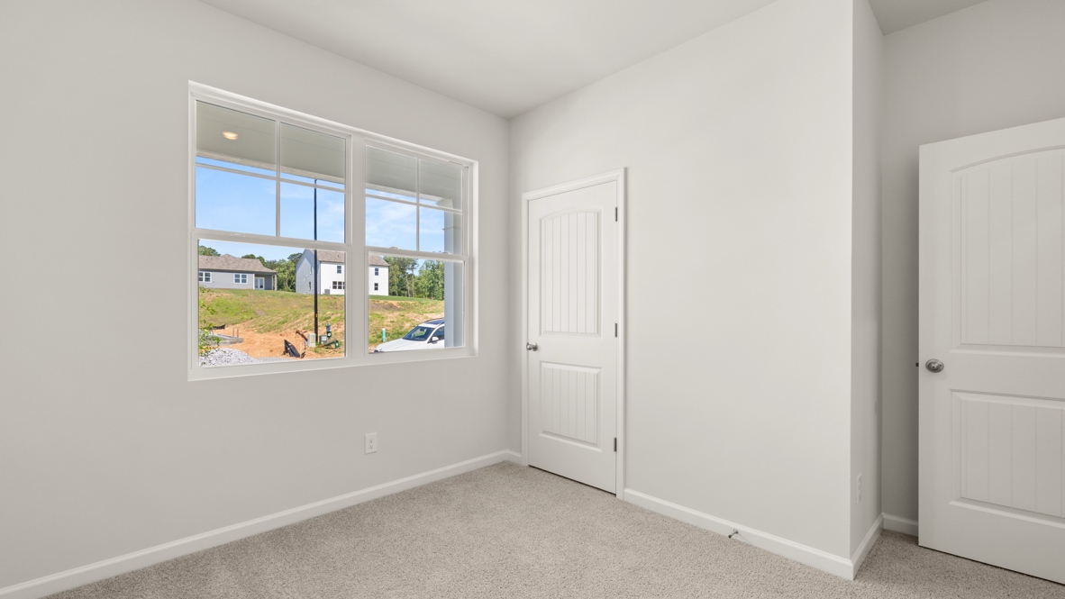 Bedroom with carpet flooring, large window, and white door with closet.