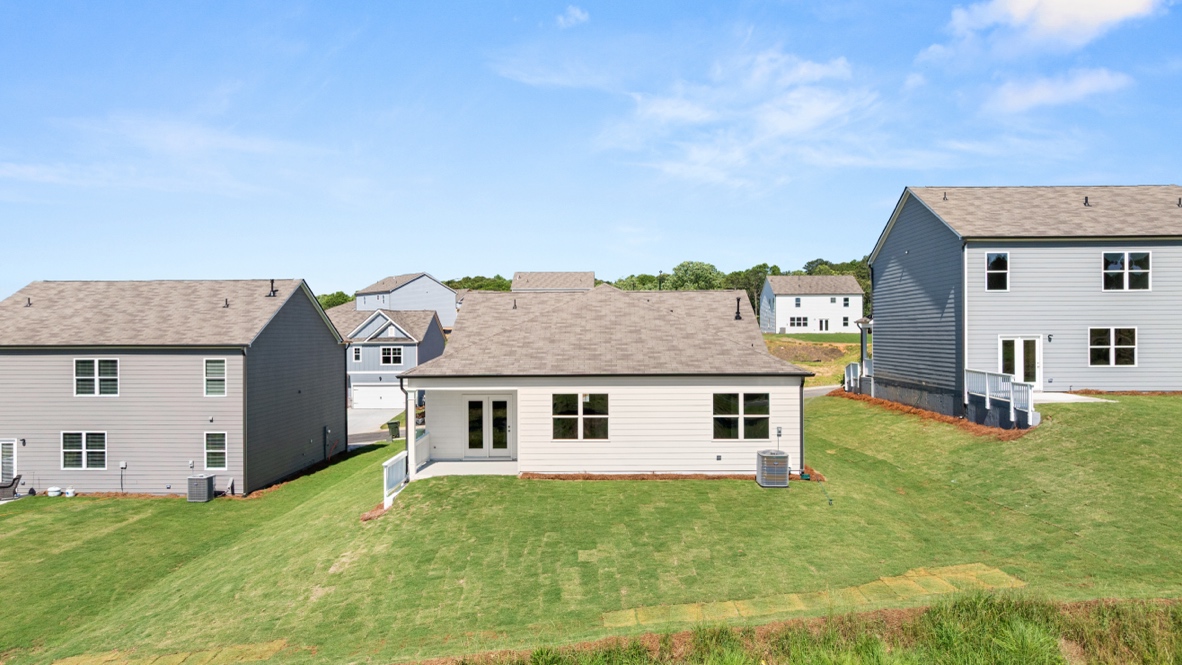 Rear view of single-story house with covered patio, windows, and backyard.
