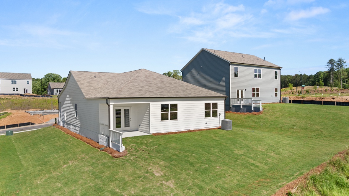 Rear angled view of single-story house with patio, grass yard, and neighboring homes.