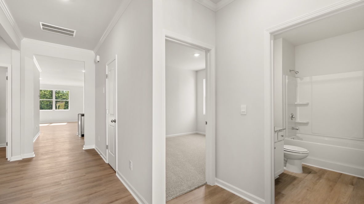Hallway with wood flooring, bedroom entrance, and bathroom with tub and toilet.