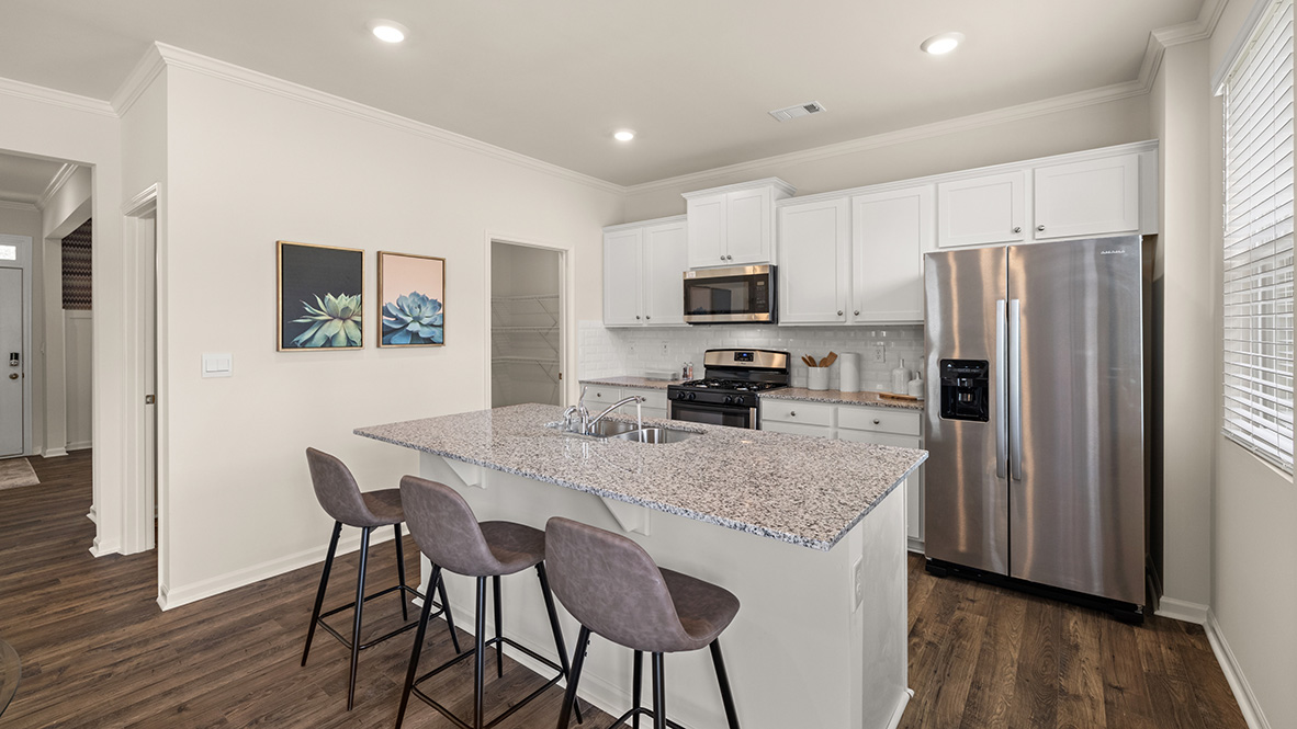 Open-concept kitchen with island sink, white cabinets, stainless steel appliances, and a single kitchen window and a view of the pantry.