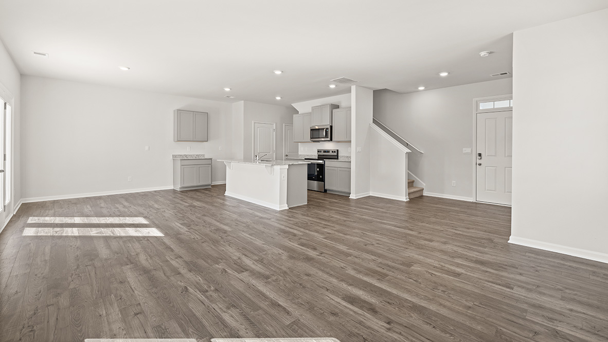 Spacious open-plan living area with wooden floors, white walls, and recessed lighting. Modern kitchen with an island, gray cabinets, and stainless steel appliances.