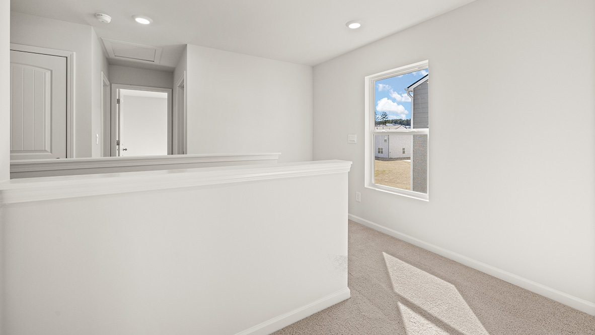 Bright hallway in a house featuring white walls, beige carpet, and natural light from a window. A closed door leads to another room, conveying a clean, modern feel.
